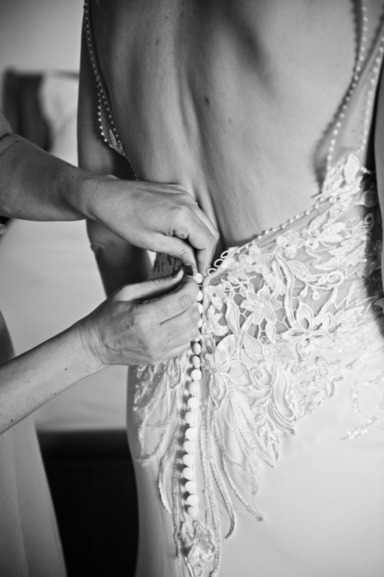 B&W Documentary photo of bride having her wedding dress done up.