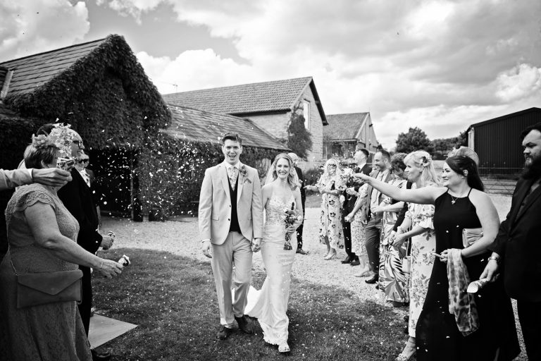 B&W photo of guests throwing confetti at the bride and groom..