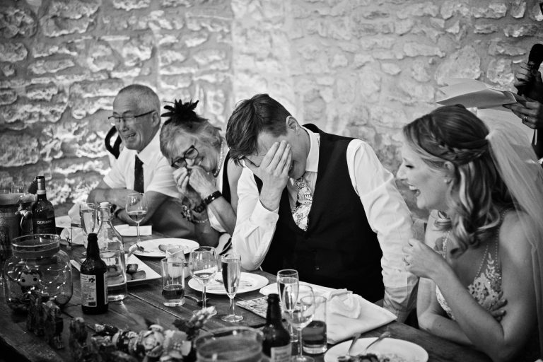 B&w photo of groom with his head in his hands during the wedding speech.