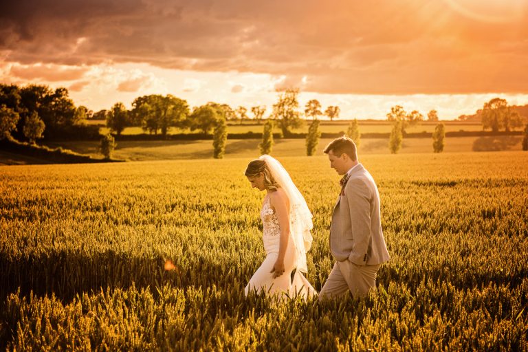 Bride and groom walk through a wheat field at Huntsmill Farm at sunset.