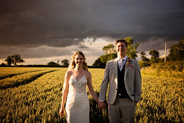 Bride and groom hold hands in a wheat field.