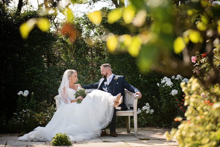 Relaxed wedding photograph of bride and groom sitting on a garden bench