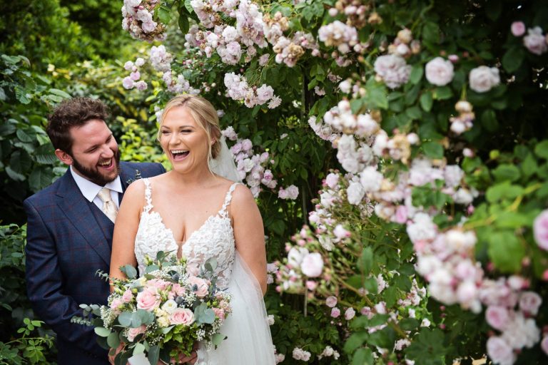 Fun and relaxed photo of bride & groom laughing in rose garden at Kingscote Barn