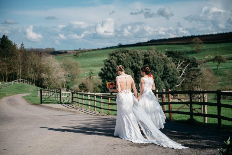Bride and bride walk off hand in hand with Cotswold countryside