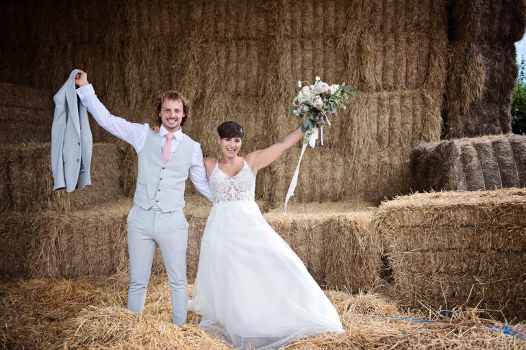 Bride and groom playing on hay bales at Kingscote Barn