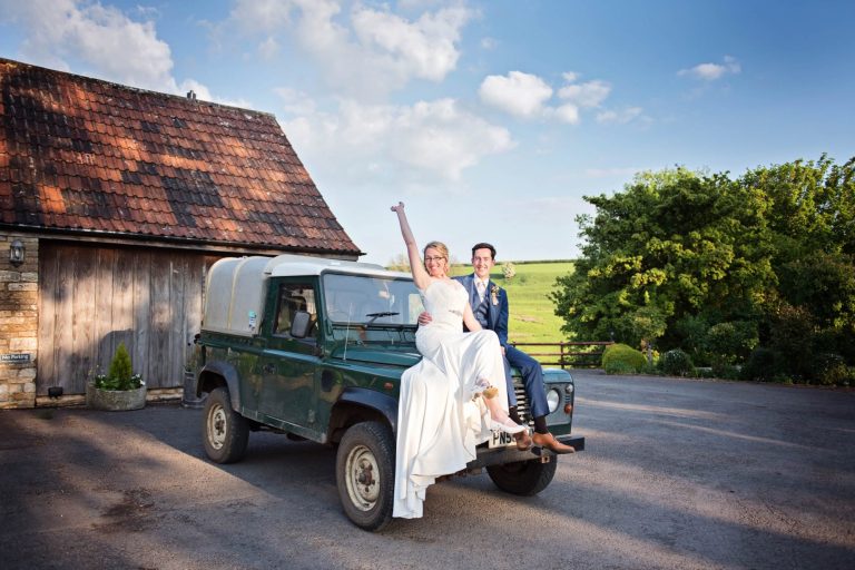 Natural light wedding photo at Kingscote Barn of Bride and groom on a landrover
