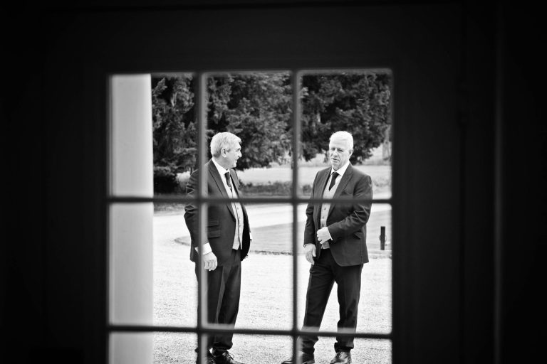 Candid photo of wedding guests (father of the groom) through a stane glass window.