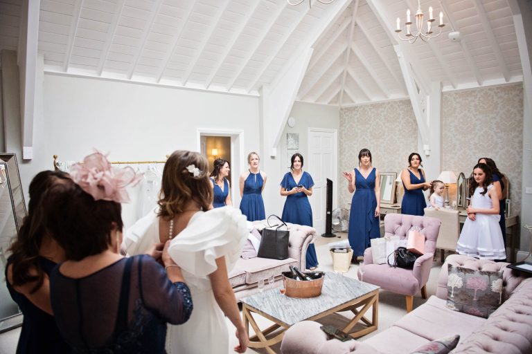 Candid photo of bride getting ready with bridesmaids watching on.