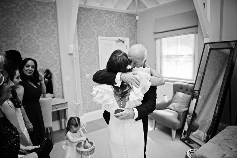 B&W documentary image of bride hugging her father as he sees her for the first time.