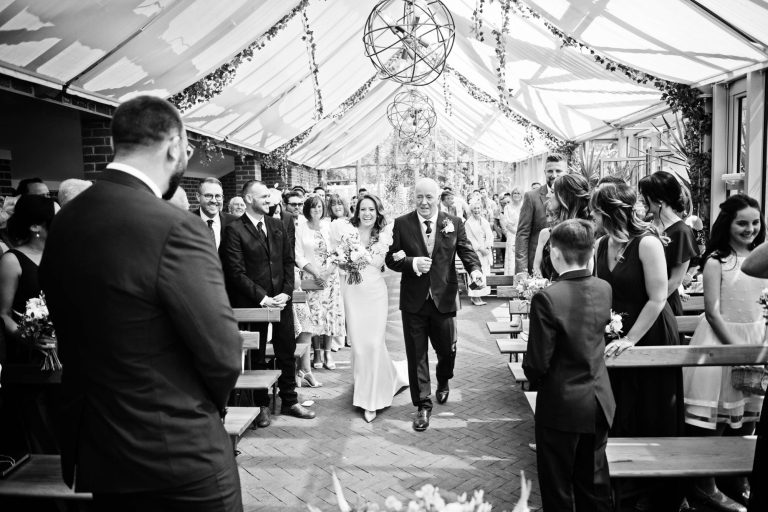 B&W storytelling photo of the bride and her father walking down the wedding isle at Syrencot.