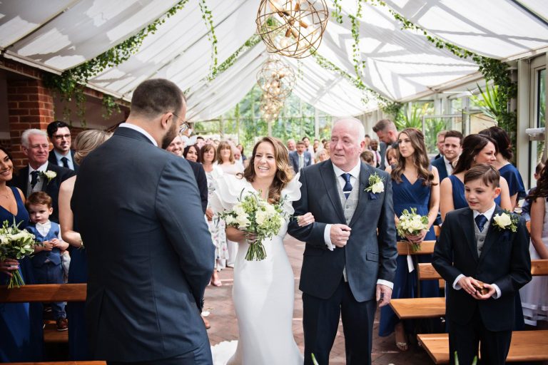 Bride walks arm in arm with father of the bride as they meet the groom during the wedding at Syrencot.