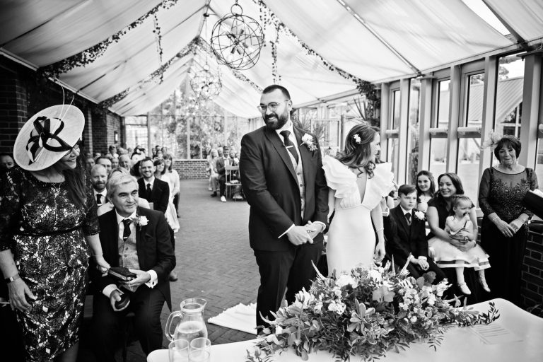 B&W documentary photo of witnesses standing up during the wedding at Syrencot.