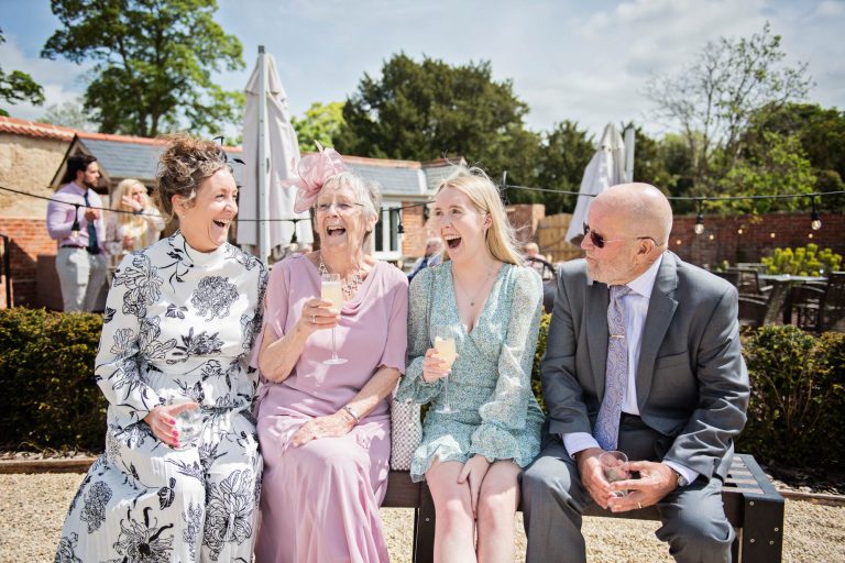Great candid photo of wedding guests laughing on a bench together.