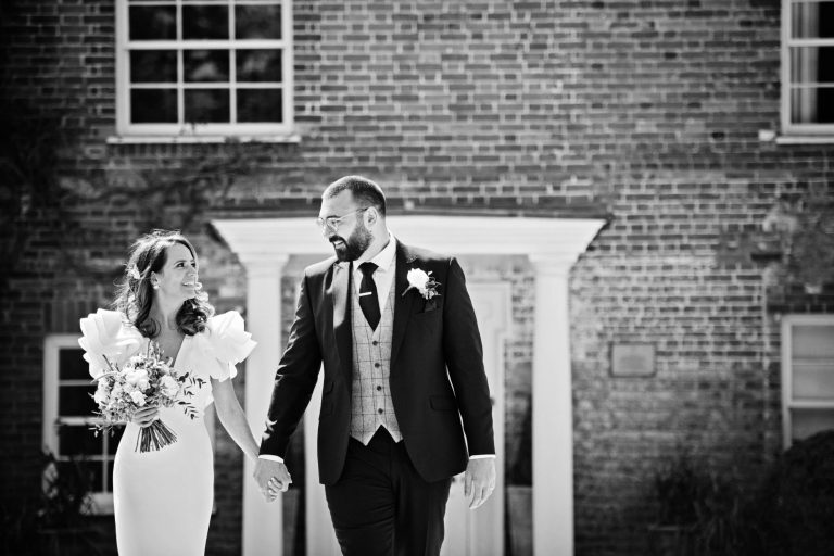 Classic b&W photo of bride and groom holding hands looking at each other with Syrencot House in the background.