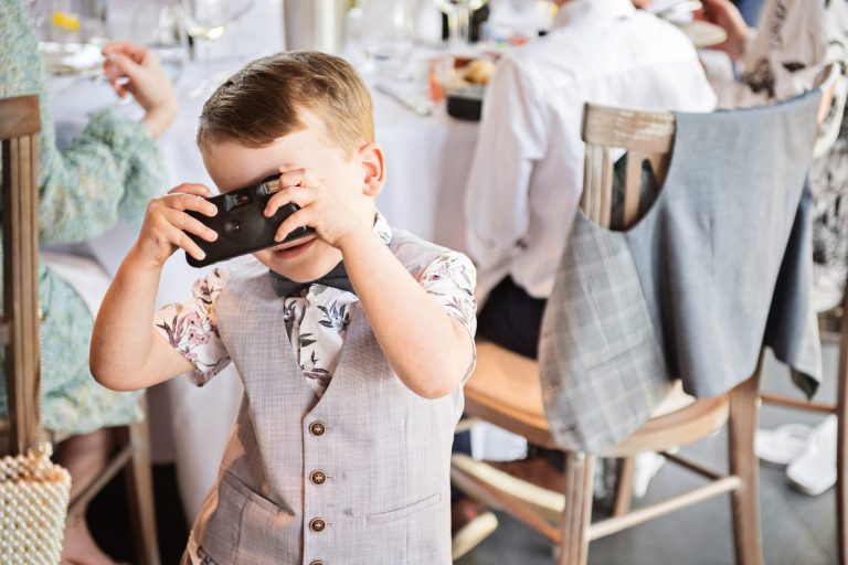 Candid photo of kids taking a photo of the photographer during the wedding breakfast.