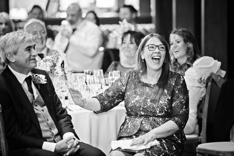 B&W photo of mother of the bride laughing during speeches.