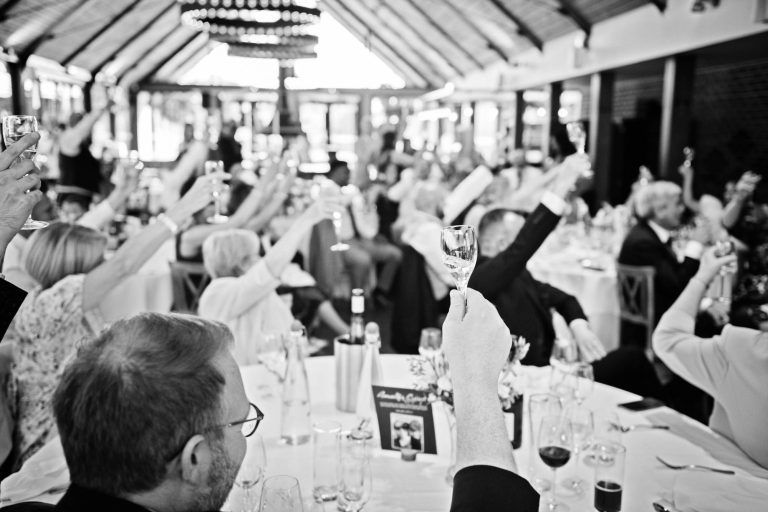 B&W photo of guests raising their glasses at end of speeches.