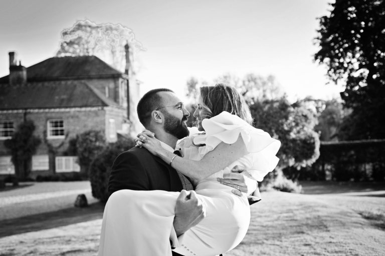 B&W fun photo of the groom carrying his bride out in the grounds at Syrencot.