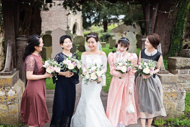 Bride and Bridesmaids stand and smile together. Candid photograph by Blooming Photography.