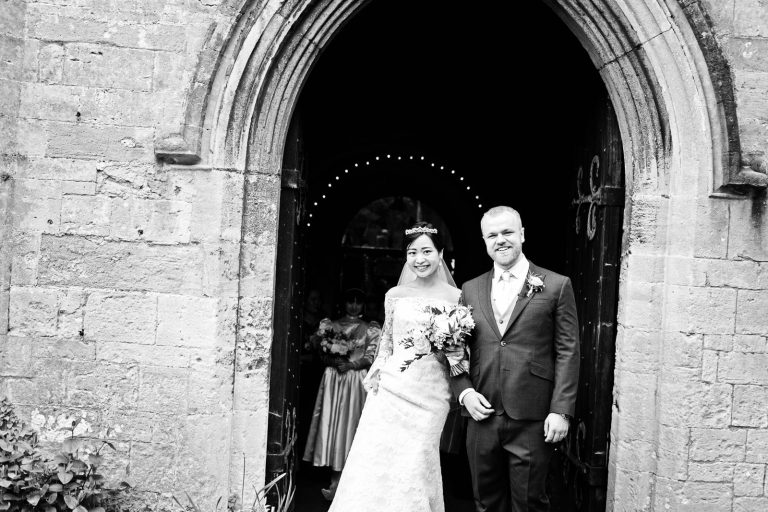 Bride and groom exit the church. Story telling black and white photograph by Blooming Photography.