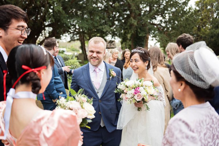 Bride and groom chat and exchange stories in the church grounds. Candid photograph by Blooming Photography.