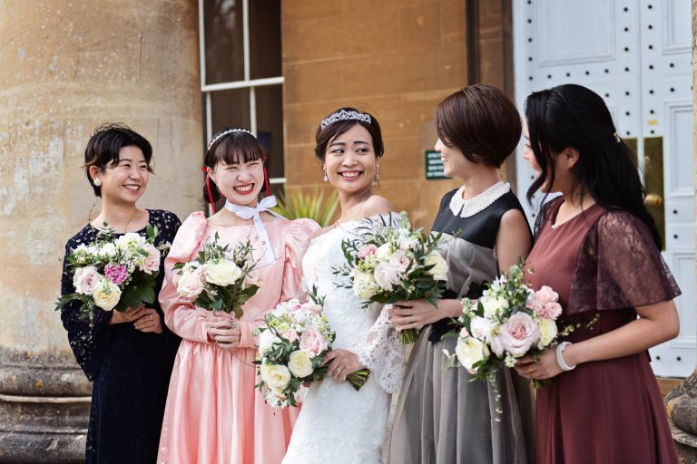 Fun photograph of bride and bridesmaids standing on the steps of Leigh Court, Bristol, holding their wedding flowers. Candid photograph by Blooming Photography.