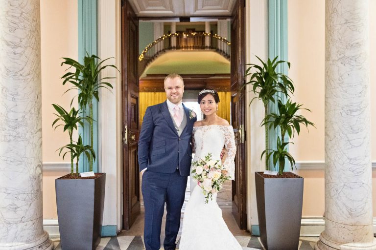 Landscape photo of bride and groom standing in the front reception hall at Leigh Court, Bristol. Candid photograph by Blooming Photography.