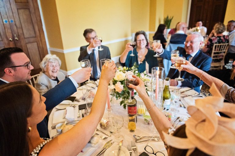 Guest raise their glasses to cheer at the wedding breakfast at Leigh Court, Bristol. Phot by Blooming Photography.