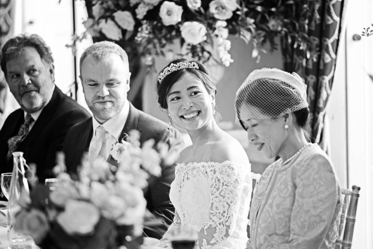 Candid black and white photo of bride smiling during speeches photo by Blooming Photography.