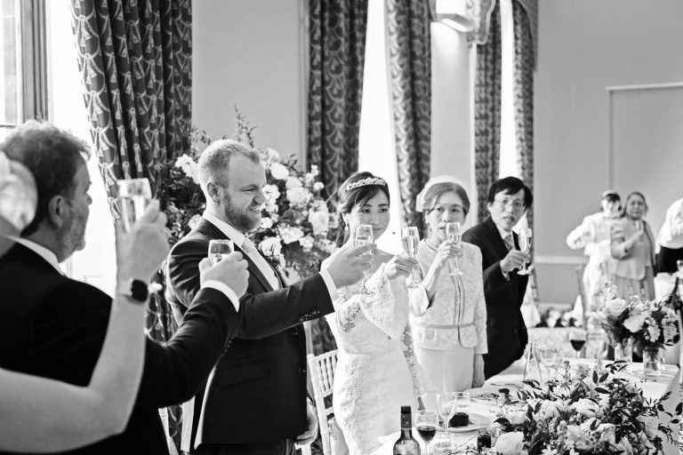 Cheers! Guest raise their glass to toast a speech in the library at Leigh Court, Bristol. Black and white Photo by Blooming Photography.