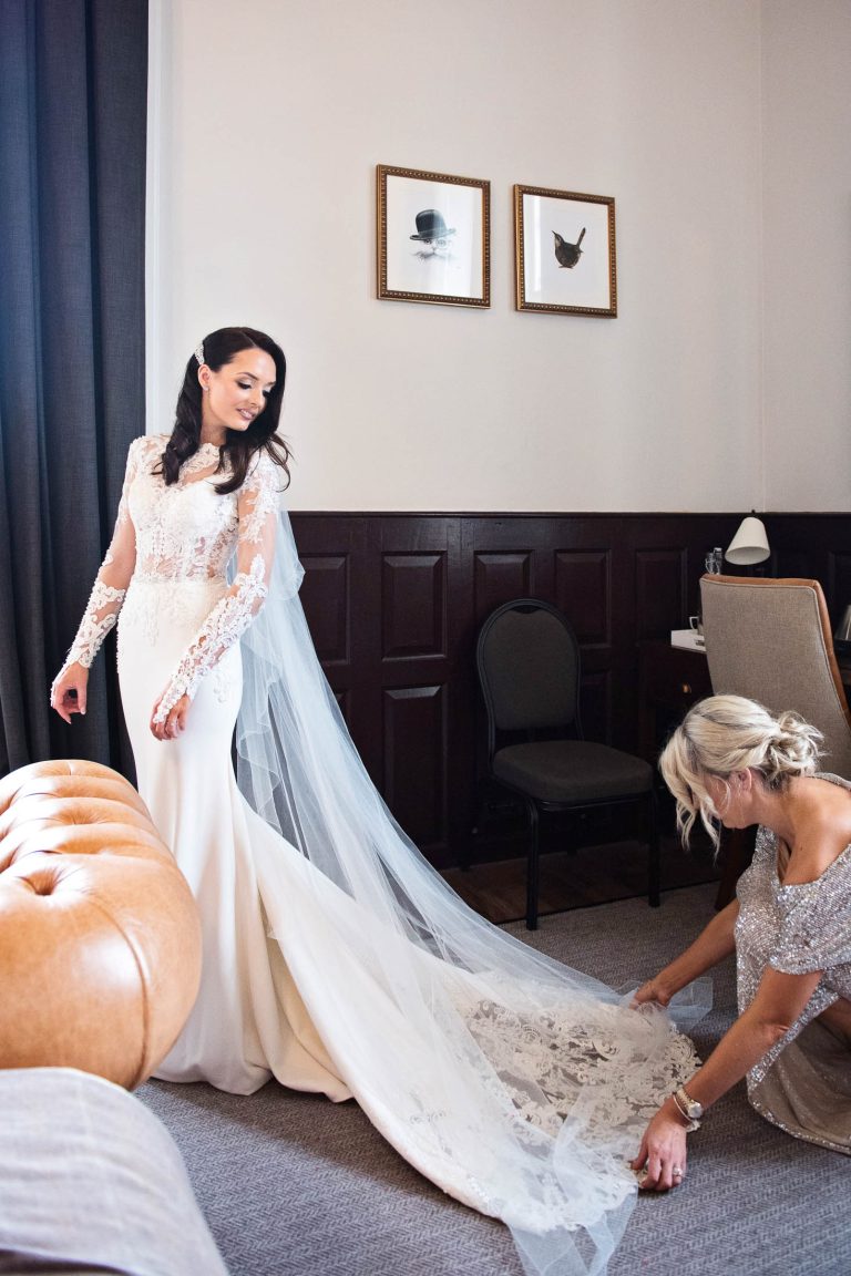 Portrait photo of bride. Bridesmaid laying the dress out.
