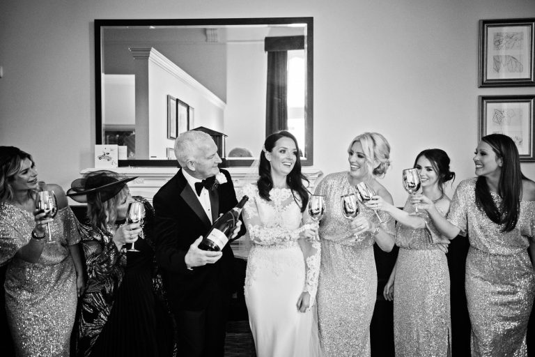 B&W photo of the bride, her father and and the bridesmaids raising a glass together.