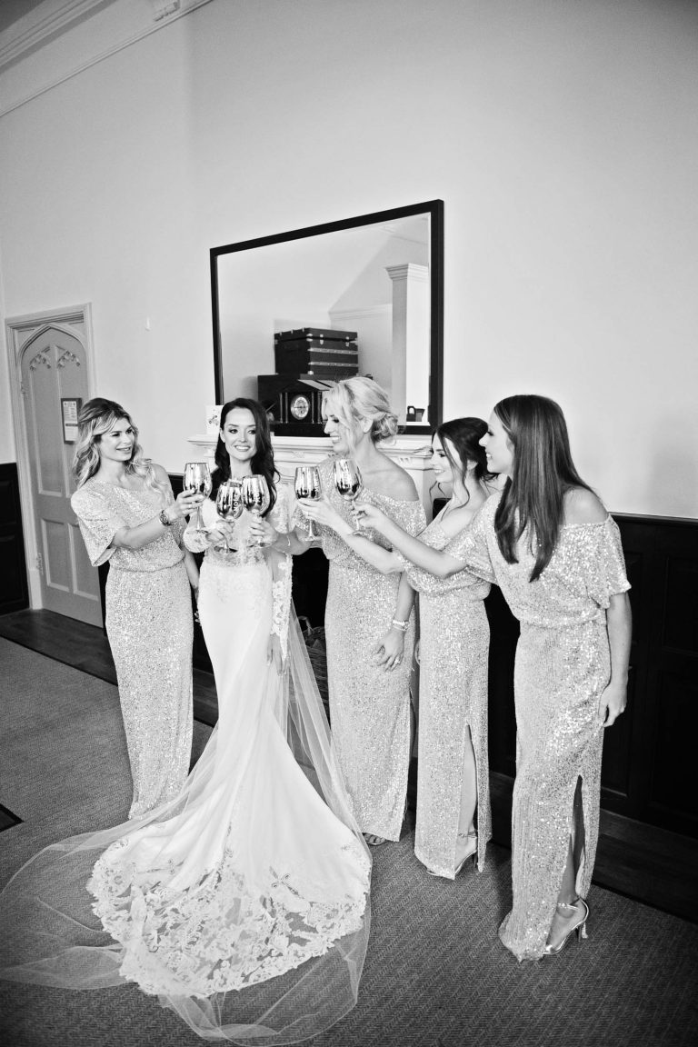 B&W portrait photo of the bride and her bridesmaids raising a glass together.