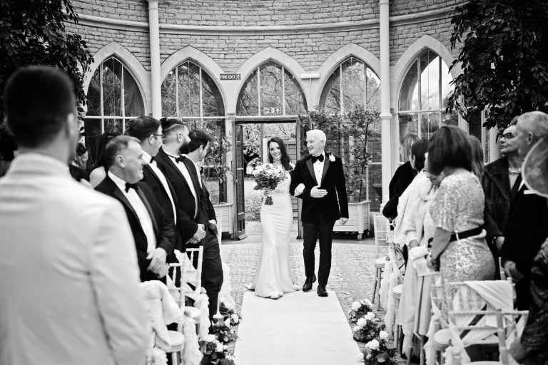 B&W documentary photo of bride as she walks down the isle in the Orangery at Tortworth Court.