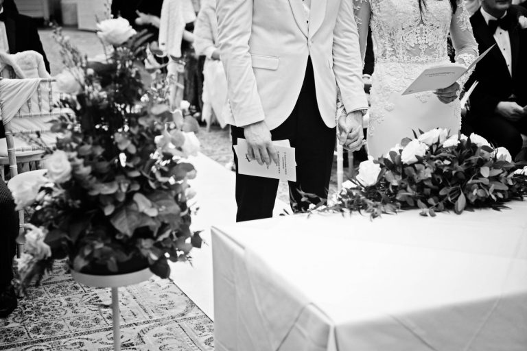 B&W candid photo of the bride and groom holding hands.