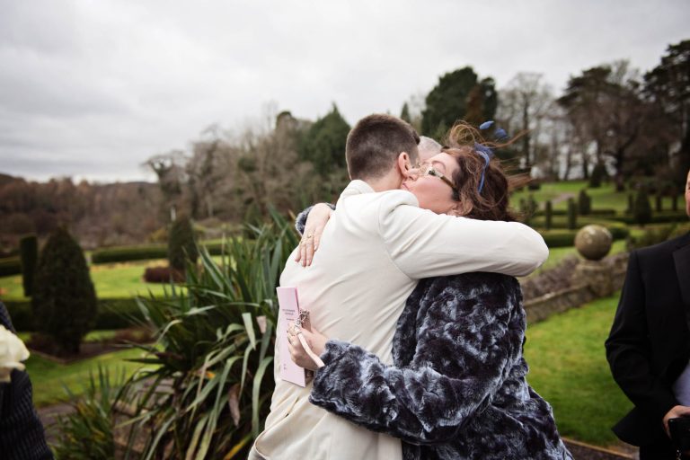 Candid photo of groom getting hugged by wedding guest.