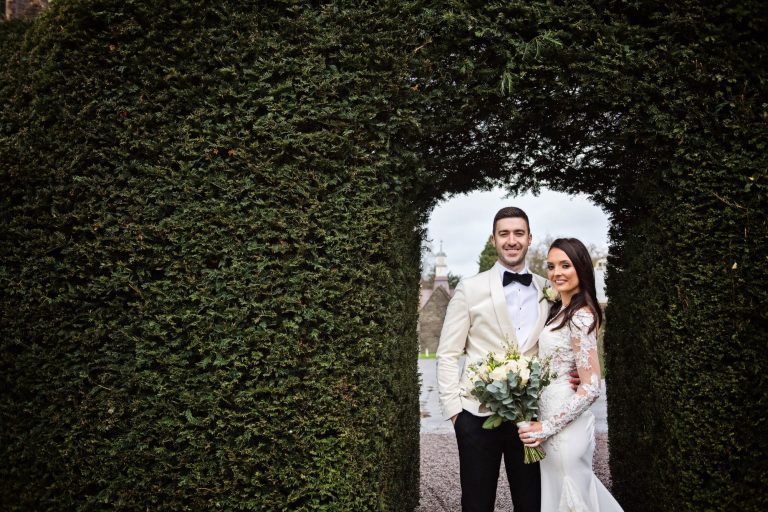 Bride and groom stand in the opening of the yew hedge at Tortworth Court.