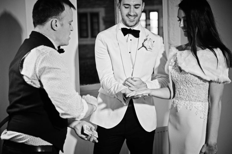 B&W candid photo of bride and groom with magician.