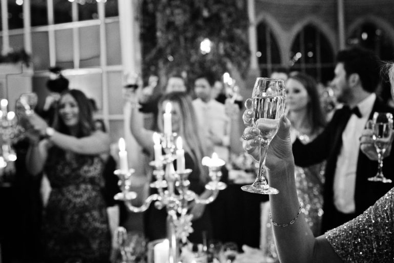B&W candid photo of wedding guests raising their glasses at the end of wedding speeches at Tortworth Court.
