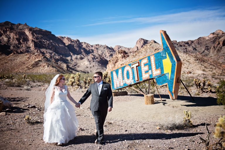 Bride and groom walk away from a very large old Las Vegas Motel and Arrow sign in the Nevada Desert. Photograph by Blooming Photography, photographed at Nelson Ghost Town.