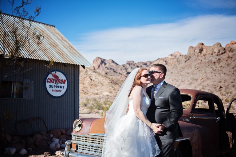 A bride and groom kiss in front of an old rusting Chevrolet, Photograph by Blooming Photography, photographed at Nelson Ghost Town.