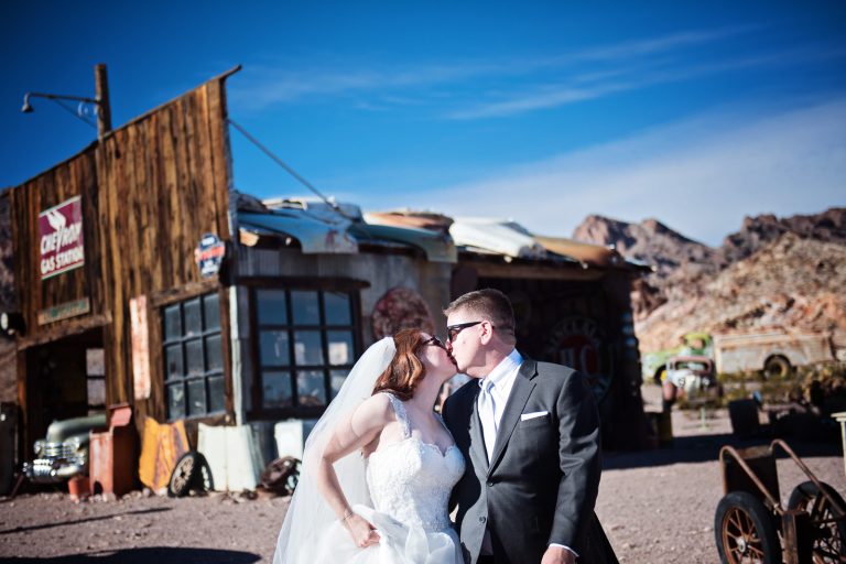 Bride and groom walk and in hand away from an old gas station. Photograph by Blooming Photography, photographed at Nelson Ghost Town.