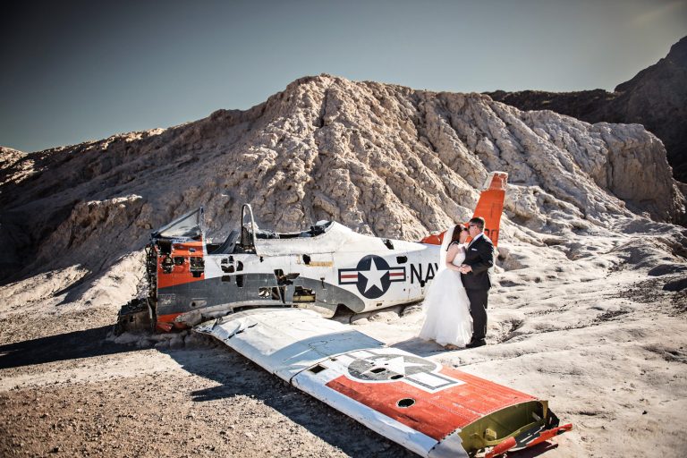 Bride and groom kiss in the Nevada Desert next to an old US Navy Fighter Plane. Photograph by Blooming Photography, photographed at Nelson Ghost Town.