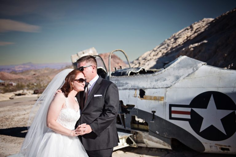 Bride and groom kiss in the Nevada Desert next to an old US Navy Fighter Plane. Photograph by Blooming Photography, photographed at Nelson Ghost Town.
