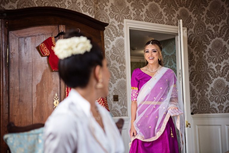 Bridesmaid walks into bridal suite, smiling at bride, candidly photographed by Blooming Photography