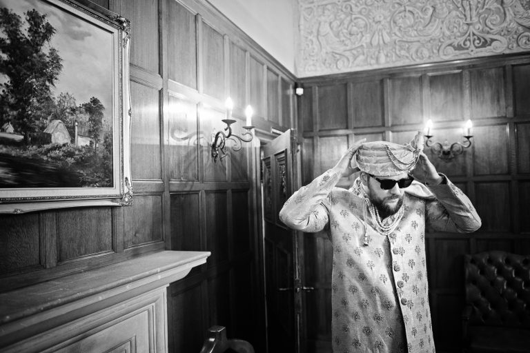 Groom putting on his indian headpiece at North Mymms Park, candidly photographed by Blooming Photography