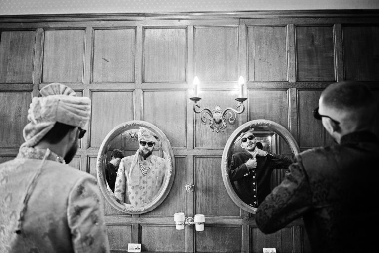 Groomsmen putting on their Indian headpiece at North Mymms Park using mirrors, photo b&w, candidly photographed by Blooming Photography