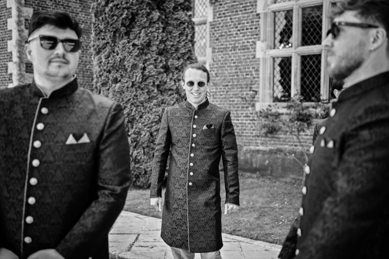 Black and white candid image of three groomsmen in Indian wedding attire, at North Mymms Park, candidly photographed by Blooming Photography.