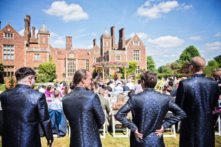 Groomsmen look on to the ceremony at North Mymms Park, candidly photographed by Blooming Photography.