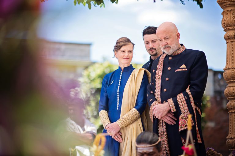 Mother and father of the groom hold hands poignantly at North Mymms Park, candidly photographed by Blooming Photography.